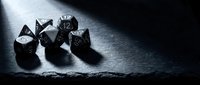 Set of black polyhedral gaming dice on dark textured surface with dramatic lighting creating shadows for tabletop role-playing games and board game adventures.
