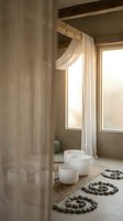 Serene meditation room with white singing bowls and stone spirals on natural fiber rug, featuring flowing curtains and warm sunlight through windows.