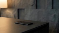 Sleek black smartphone resting on dark wooden desk in modern minimalist office space with concrete wall backdrop and warm lighting for tech and workspace concepts.