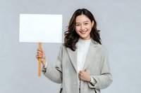 Smiling Asian businesswoman in light gray blazer holding blank protest sign against neutral background for mockup or message display.