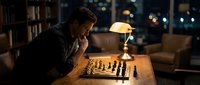 Focused man playing chess alone in cozy home library with warm lamp lighting during evening hours for strategic thinking and mental challenge.