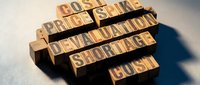 Wooden letter blocks spelling business terms like cost, price, profit, devaluation, shortage, and cash arranged on textured surface with dramatic shadows.