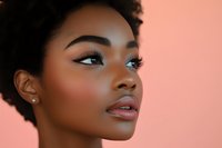 Young African American woman with natural curly hair and flawless glowing skin against coral background, showcasing professional makeup and side profile pose.