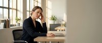 Stressed businesswoman experiencing headache while working on laptop in modern office environment during busy workday.