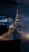 Glowing golden light trails forming upward arrow above laptop displaying financial charts and growth statistics in modern dark office environment.
