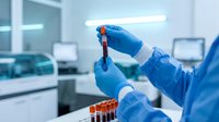 Medical laboratory technician in blue protective gloves holding blood sample test tube in modern clinical research facility for diagnostic testing.
