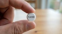 Hand holding white placebo pill tablet between fingers in medical research clinical trial pharmaceutical testing environment for drug development studies.