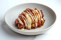 Grilled chicken breast drizzled with creamy white sauce and caramelized glaze served on white ceramic plate, gourmet restaurant presentation on marble surface.