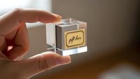 Hand holding transparent glass cube with golden gift box label, luxury packaging concept for premium products and elegant presentation design.