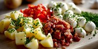 Fresh ingredients for traditional Spanish tapas arranged on wooden board with diced potatoes, chorizo, red peppers, mozzarella balls, and fresh herbs.