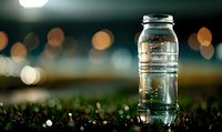 Clear plastic water bottle on grass at night with bokeh lights in background, highlighting hydration during outdoor activities.