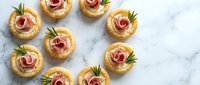 Elegant appetizer canapes with rolled ham roses and fresh herbs arranged on marble surface for catering events and gourmet entertaining occasions.