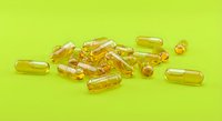 Golden yellow vitamin capsules and soft gel supplements scattered on bright lime green background for health and wellness concepts.