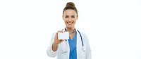 Young female healthcare professional with light skin tone and blonde hair styled in a bun, wearing white medical coat and stethoscope, holding blank business card for branding and contact information.