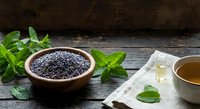 Black chia seeds in wooden bowl with fresh mint leaves and herbal tea on rustic wooden table. Healthy superfood ingredients for wellness nutrition.