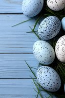 Speckled white quail eggs arranged with fresh green grass blades on rustic blue wooden planks, creating natural Easter or spring composition with copy space.