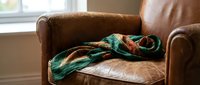 Cozy brown leather armchair with colorful knitted blanket by sunny window creating warm comfortable living room atmosphere for relaxation and home decor.
