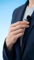 Professional businesswoman adjusting small lavalier microphone on navy blue suit jacket for interview or presentation recording.