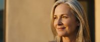 Mature woman with long gray hair and fair complexion smiling indoors with warm lighting, suitable for healthcare, wellness, lifestyle and corporate business concepts.