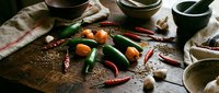 Fresh green and red chili peppers with spices on rustic wooden cutting board in moody kitchen setting for cooking and culinary preparation.