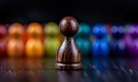 Wooden chess pawn piece against colorful blurred background with rainbow spectrum colors, dramatic lighting on dark surface creates artistic composition.