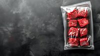 Fresh raw beef cubes vacuum sealed in plastic package on dark concrete background with copy space, ready for sous vide cooking or freezer storage.