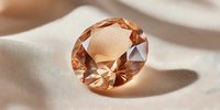 Sparkling orange gemstone with brilliant cut facets casting shadows on soft beige fabric surface in warm natural lighting for luxury jewelry design.