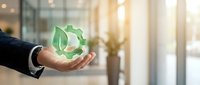 Businessman hand holding green recycling symbol in modern office environment representing corporate sustainability and environmental responsibility.