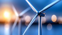 Wind turbines against blurred blue sky and setting sun, creating clean renewable energy with bokeh light effects in foreground, environmental concept.