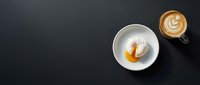 Overhead view of white ceramic cup with espresso and caramel swirl beside latte with latte art on dark surface, ideal for cafe menu design and coffee shop marketing materials.