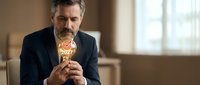 Mature Caucasian businessman in dark suit holding golden trophy award in office interior, corporate success achievement concept for business presentations.