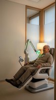 Senior Caucasian man receiving modern light therapy treatment in medical chair at wellness clinic for health rehabilitation and recovery.