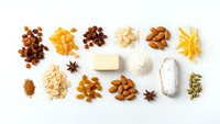 Assorted nuts, dried fruits, spices and baking ingredients arranged on white background. Healthy snacking and cooking essentials for recipes.
