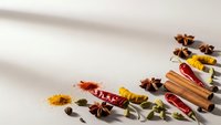 Aromatic spices and herbs scattered on white surface with warm sunlight shadows creating culinary cooking ingredients display for kitchen recipes.