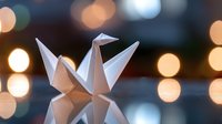 Delicate white paper crane origami on reflective surface with soft bokeh lights creating magical atmosphere. Artistic macro photography with shallow depth of field.