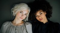 Two diverse young women with contrasting hairstyles posing together in studio portrait for fashion, beauty and lifestyle content.