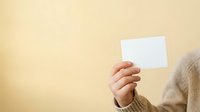 Close-up of a hand holding a blank white card against a soft yellow background, suitable for business cards, promotional materials, and marketing campaigns.