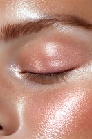 Close-up of glowing skin with shimmering makeup and glitter details on closed eyelid, showcasing dewy complexion and natural eyebrow texture for beauty and cosmetic advertising.