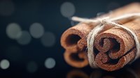 Aromatic cinnamon sticks tied with rustic twine against dark background with soft bokeh lights, macro food photography highlighting spice texture and detail.