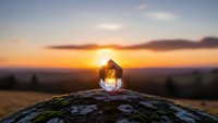 Vintage lantern glowing on moss-covered rock during golden sunset with mountain silhouettes and dramatic sky for outdoor adventure and camping themes.