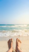 Relaxed feet with sandy toes on tropical beach with turquoise ocean waves and clear blue sky background for vacation and summer holiday concepts.