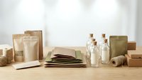 Eco-friendly packaging materials including kraft paper bags, glass bottles with cork stoppers, cardboard boxes and natural twine on wooden surface.