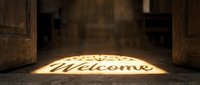Warm golden light shines through open wooden doors, projecting a Welcome sign onto a stone floor, evoking hospitality, faith, and invitation.