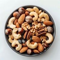 Mixed raw nuts and seeds in black ceramic bowl on white background, including cashews, almonds, walnuts, pecans and hazelnuts, top view food photography.