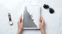 Hands holding abstract minimalist artwork with geometric shapes on marble surface, styled flat lay with watch and sunglasses for design inspiration.