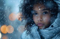 Young African American woman with curly hair in winter coat gazing thoughtfully amid falling snow and bokeh lights creating magical winter atmosphere.