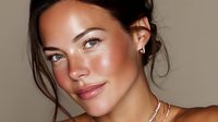 Young woman with glowing skin and natural makeup against neutral background, showcasing dewy complexion and minimal jewelry for beauty advertising.