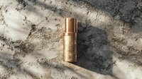 Luxury gold cosmetic bottle on concrete background with natural sunlight and shadows. Premium skincare product photography for beauty and wellness marketing.