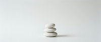 Three smooth white zen stones balanced in minimalist stack on clean background for meditation wellness spa design concepts.