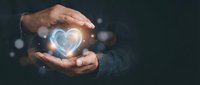 Hands protecting glowing heart symbol with light effects on dark background representing care, love, protection, healthcare and compassion concepts.